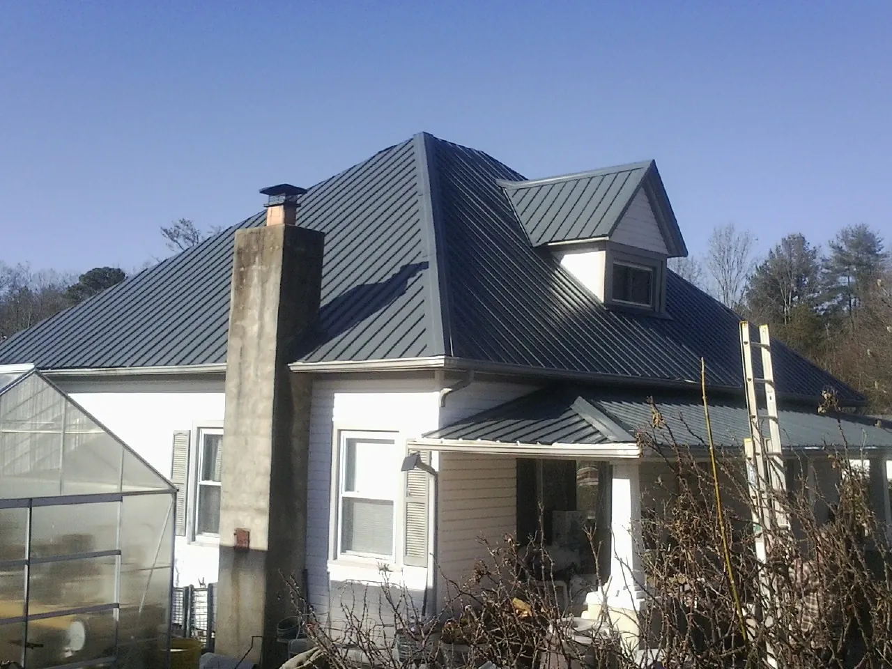 Dark blue standing seam metal roof on a white farmhouse with dormer — Slate & Tile Roof Repair by Roofing Brothers in Woodford