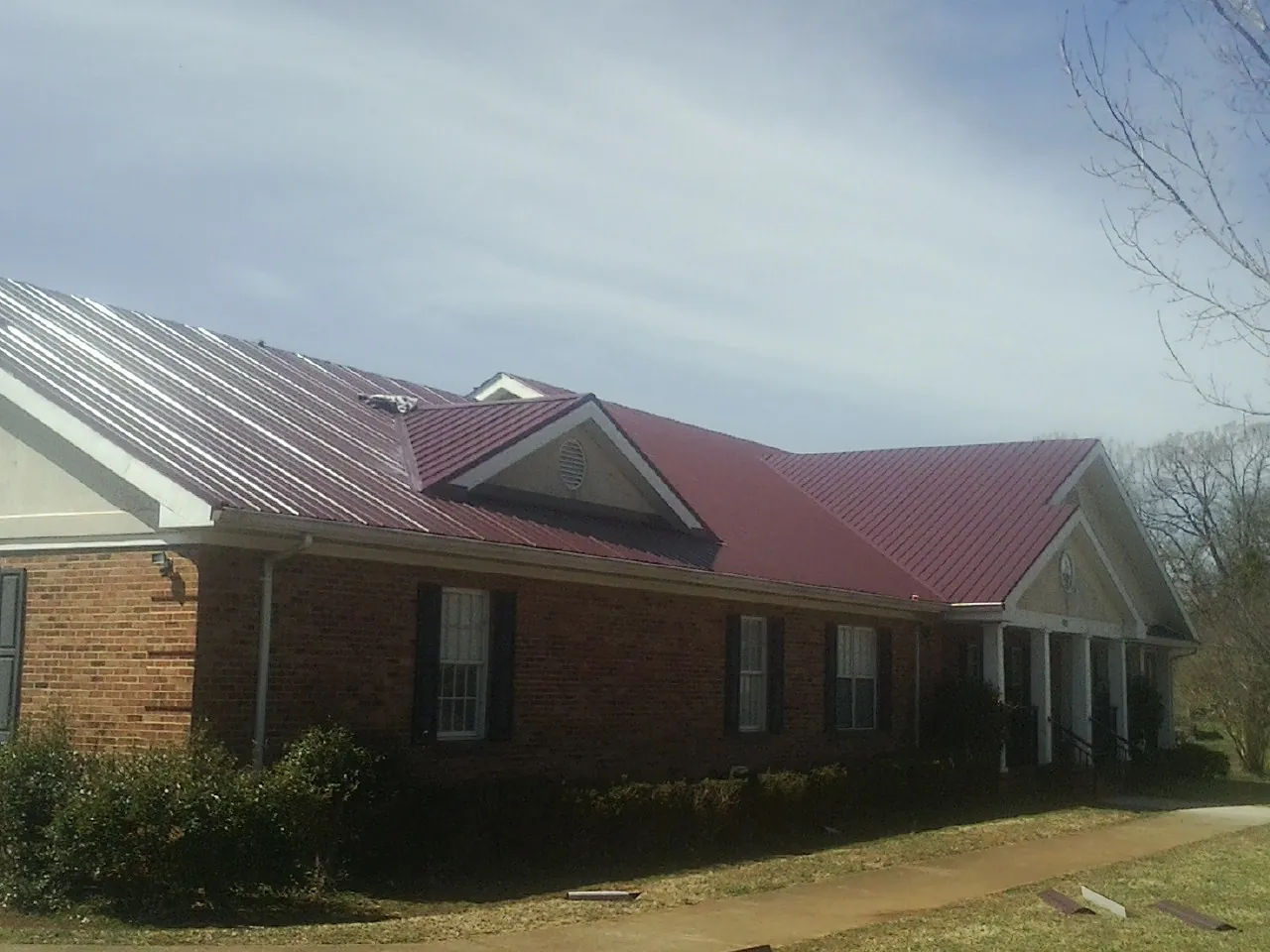 Red metal roof with gabled entries on a long brick building, from a Hail Damage Roof Repair job in Woodford