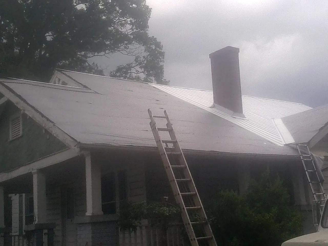 Ladders against a metal roof on an older home with a brick chimney in Woodford
