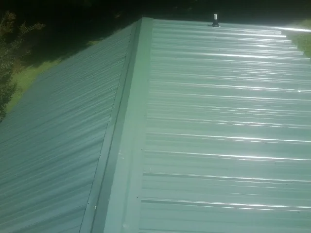 New green metal panels meeting at the ridge of a roof — Flat Roof Repair work by our crew in Woodford