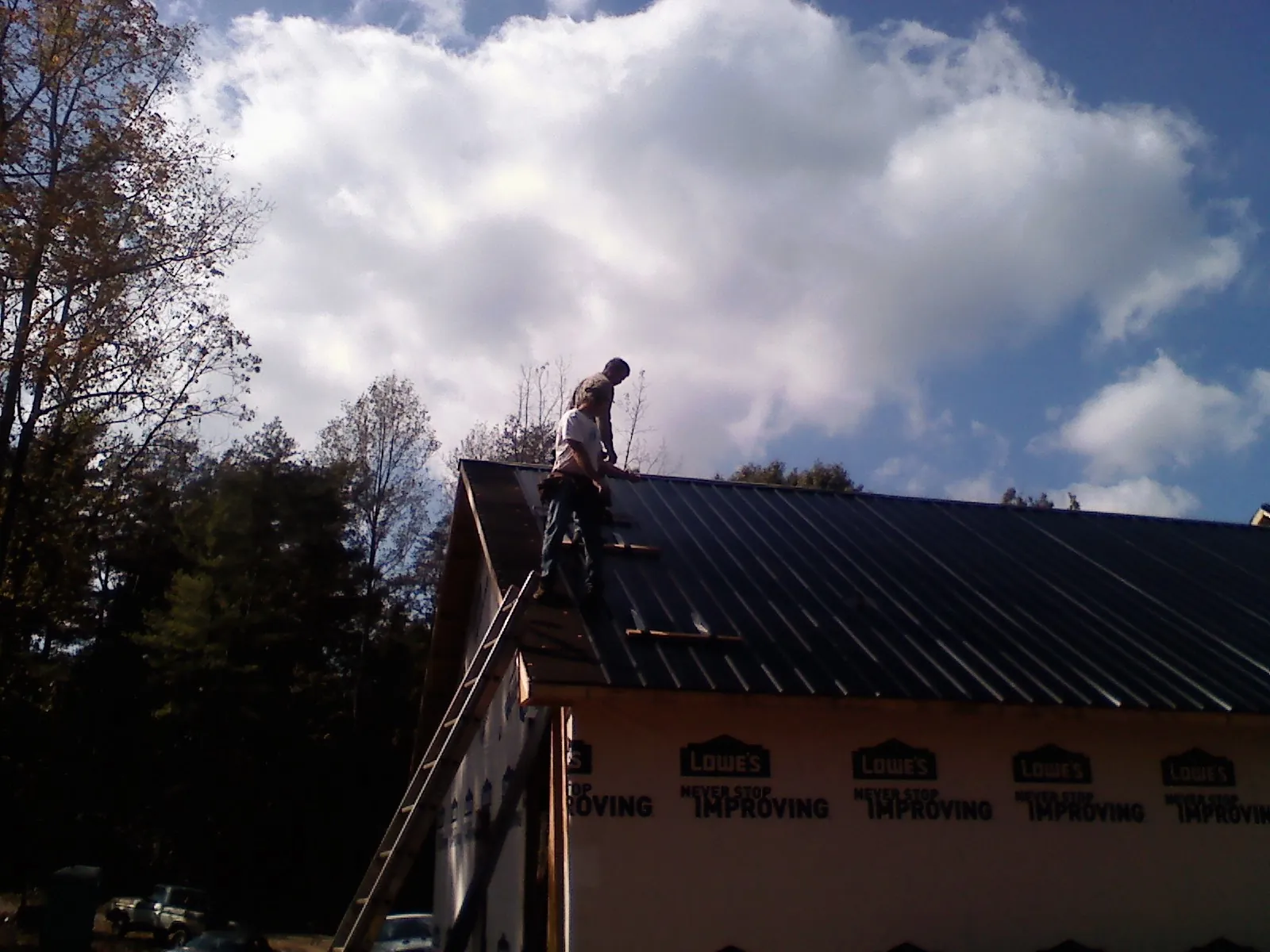 Roofer fastening dark metal panels high against a cloudy sky, from a Roof Inspection job in Woodford
