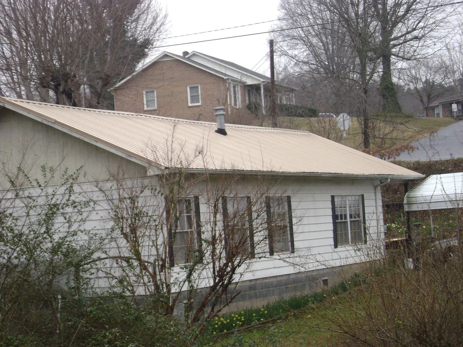 Tan metal roof on a white sided house set into a hillside — Commercial Roofing by Roofing Brothers in Woodford